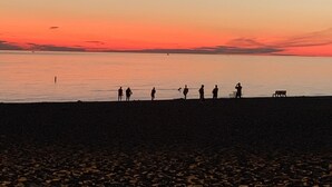 A beach at sunset with silhouettes of people and a bench.