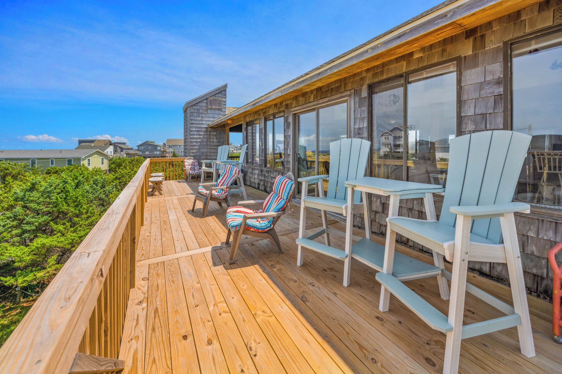 Une terrasse en bois avec des sièges extérieurs, de grandes fenêtres et une vue sur l’océan.