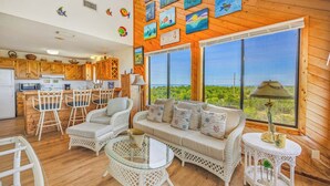 A cozy room with wicker furniture, a sofa with cushions, a round glass table, and a view of the sea through large windows.