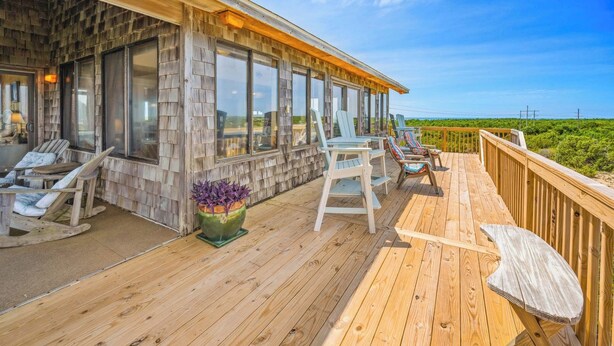A wooden deck with outdoor seating, a large windowed room, and a view of the landscape.
