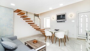 Un salon moderne avec un escalier, un coin repas et un téléviseur fixé au mur.