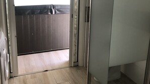 A bathroom with a glass shower enclosure, a wooden floor, and a view of a balcony with a dark wooden fence.
