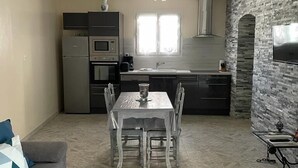 A modern kitchen with a stone accent wall, a dining area with a table and chairs, and a grey sofa with a patterned pillow.