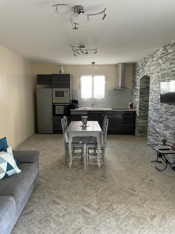 A modern kitchen with a stone accent wall, a dining area with a table and chairs, and a grey sofa with a patterned pillow.