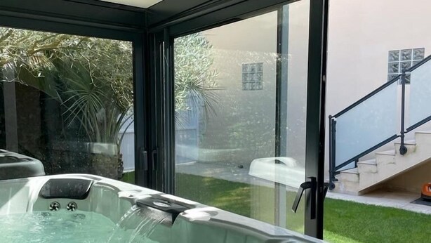 A hot tub in a covered outdoor area with a view of a garden and a staircase leading to a building.