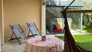 A covered patio with a table and chairs, a hanging lantern, and a view of a garden.