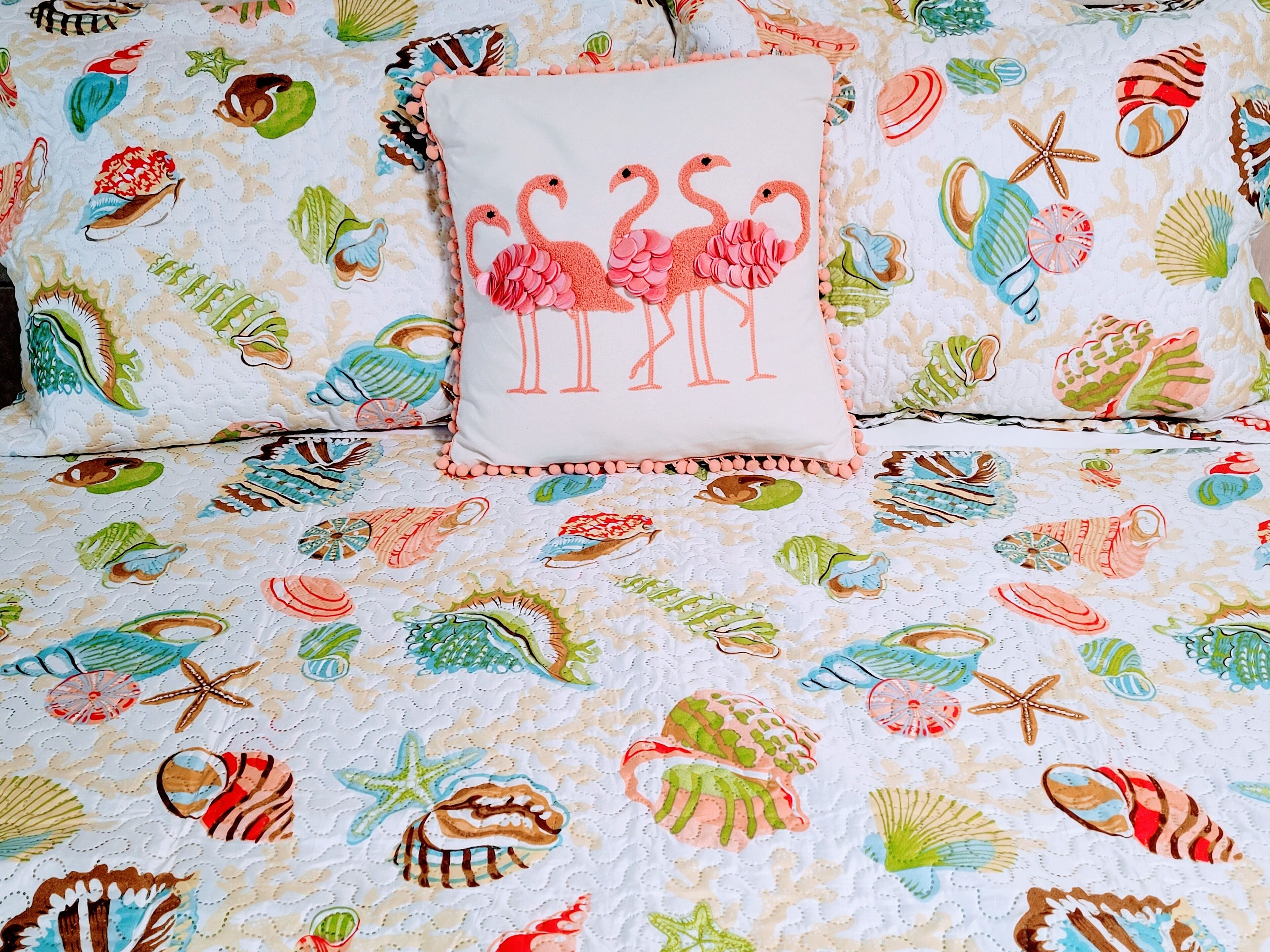 A bed with a floral and sea-themed duvet cover, a pillow with flamingos, and a decorative border.