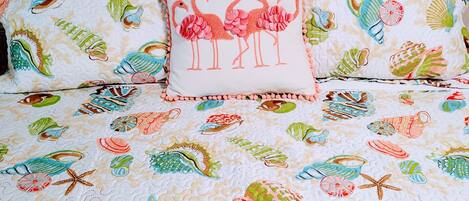 A bed with a floral and sea-themed duvet cover, a pillow with flamingos, and a decorative border.