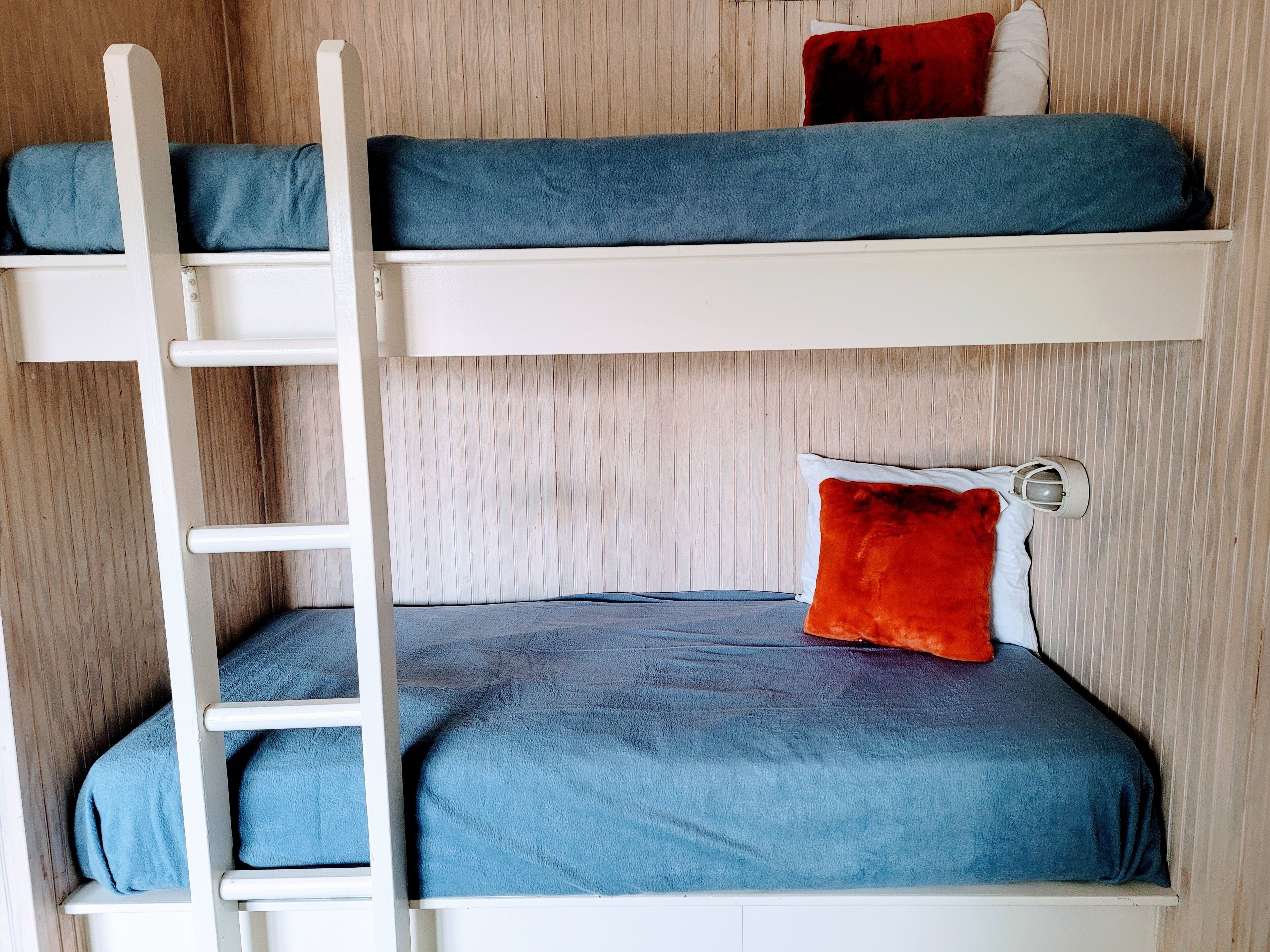 Een stapelbed met een ladder, twee kussens en een hoofdbord met een lamp.