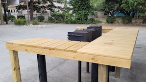Une table en bois aux pieds noirs, placée à l’extérieur sur une surface en béton.