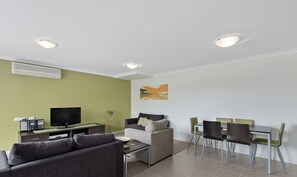 A modern living room with a flat-screen TV, a sofa, a dining table with chairs, and recessed ceiling lights. - Central one bedroom unit, Thompson Ave Cowes, security entrance, no lift (Cowes)