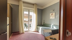 Una camera d'albergo con un letto, una scrivania, una sedia, una finestra con tende e un balcone con tavolo e sedie.