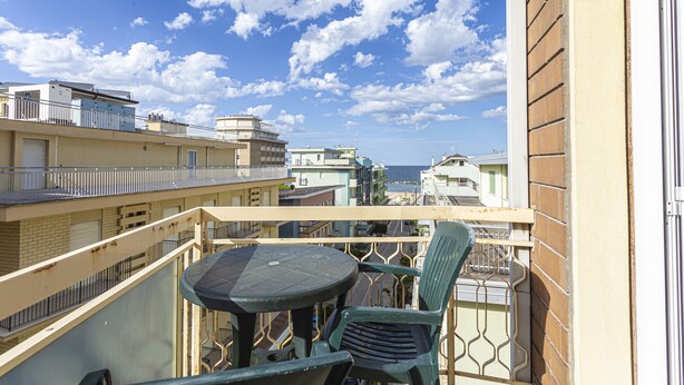 Un balcone con tavolo e sedie, affacciato su una zona costiera con edifici e il mare.