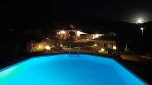 A swimming pool at night with a house in the background.