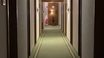 Un pasillo de hotel con alfombra verde, puertas de madera y un candelabro al final.