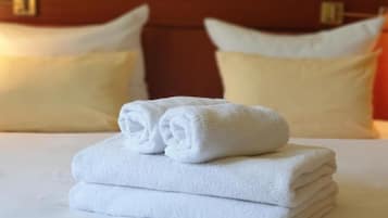 Una cama bien hecha con toallas blancas dobladas encima, un cabecero de madera y dos almohadas.