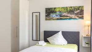 A neatly made bed with a pillow and a folded towel, a framed picture of a waterfall, a bedside lamp, and a small plant on a nightstand. - dreams Beckum (Beckum)