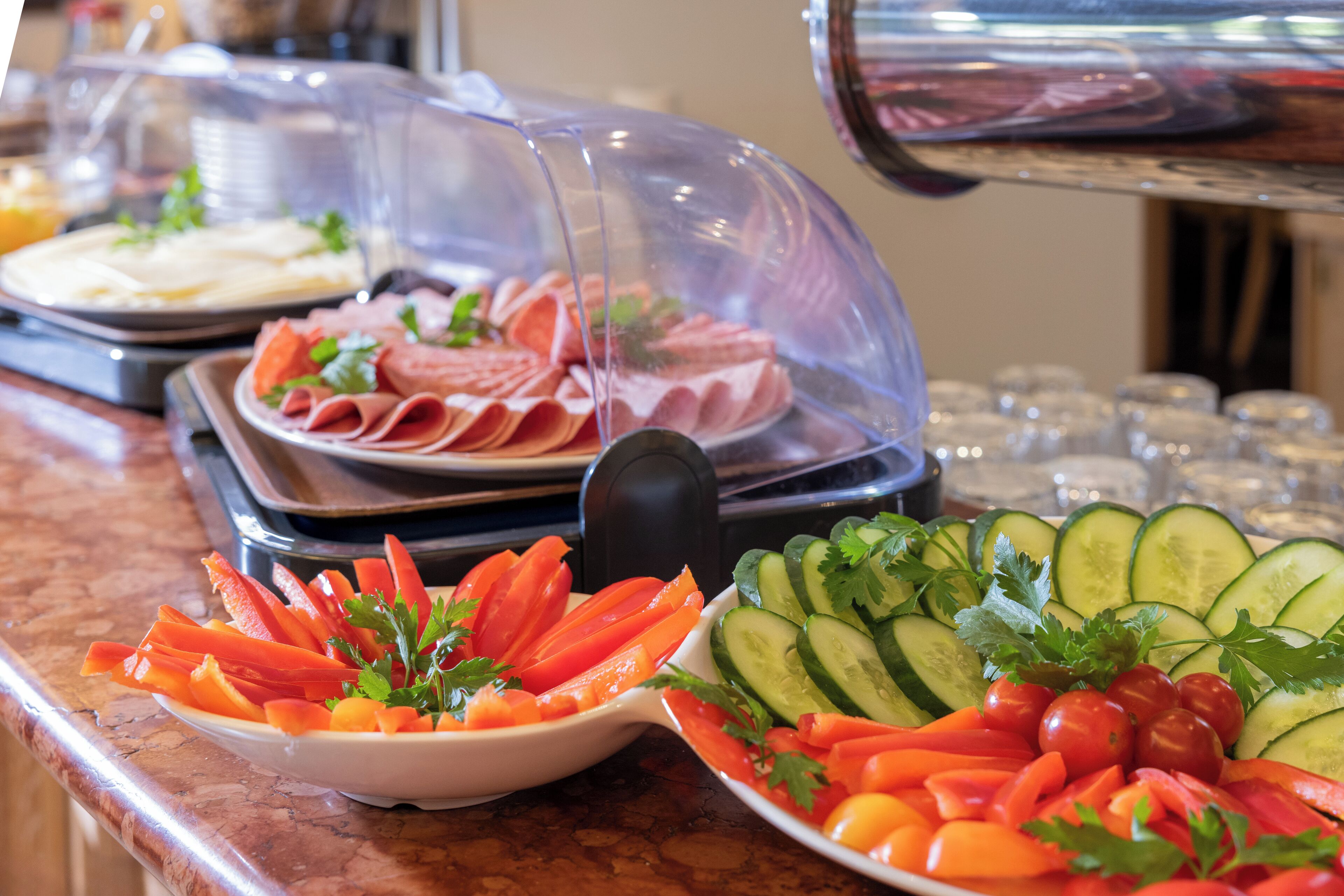 Un bufé con carnes en rodajas, verduras y una variedad de platos cubiertos con campanas de cristal.