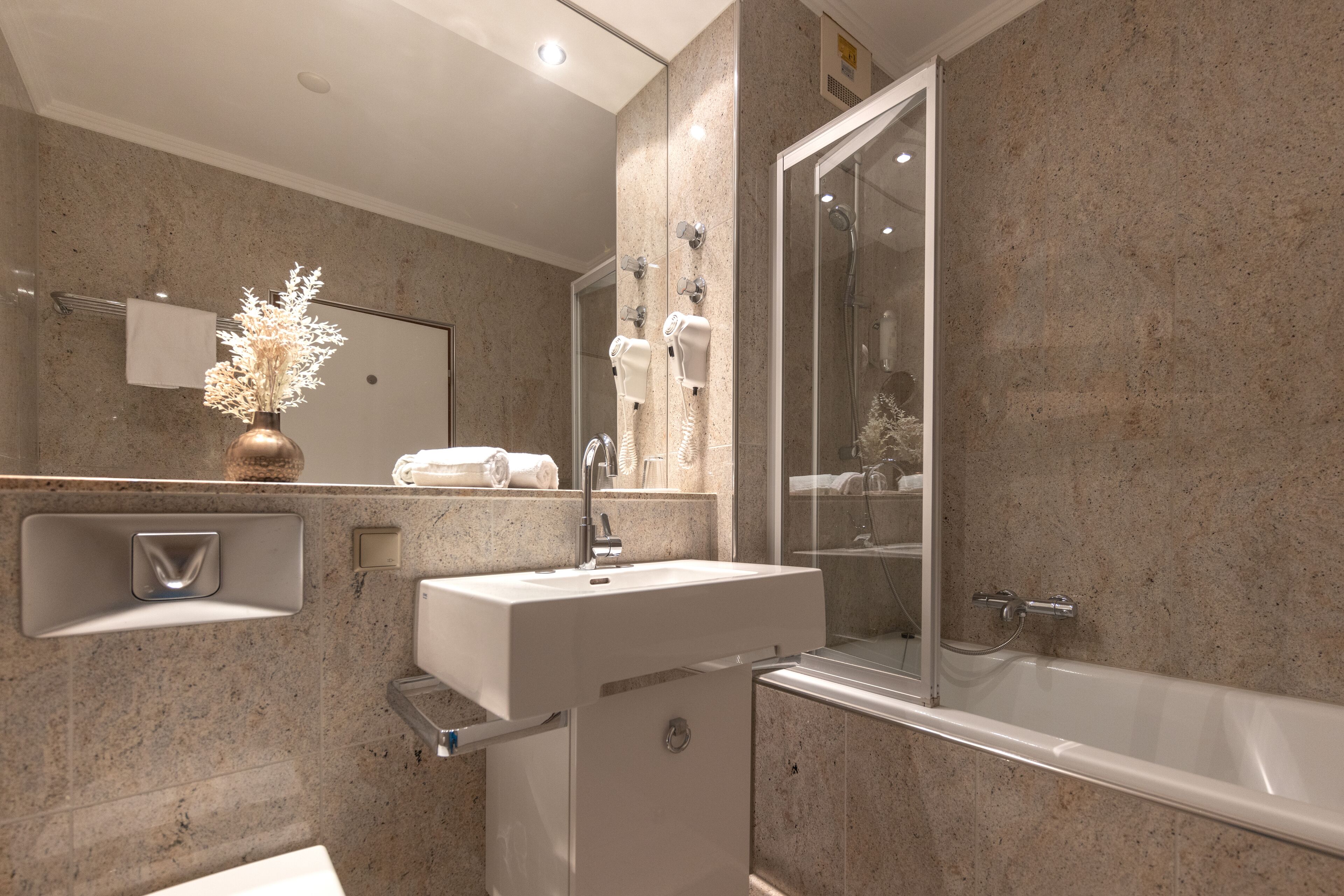 Ein modernes Badezimmer mit großem Spiegel, Waschbecken, Dusche und Handtuchhalter.