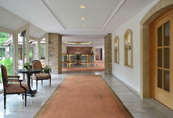Un vestíbulo de hotel con una recepción, una mesa redonda con sillas y un pasillo alfombrado.