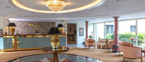 A lobby with a reception desk, a chandelier, a round table, and seating area.
