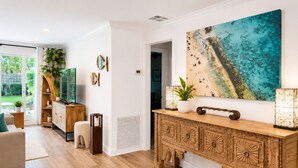 A modern living room with a wooden console table, a large abstract painting, and a view of a green outdoor area.