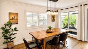 A dining area with a wooden table, black chairs, a hanging light fixture, and a window with blinds.