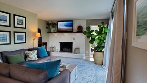 Una sala de estar con un sofá marrón, una chimenea, un televisor y cuadros en la pared.