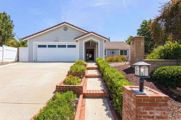 A single-story house with a garage, a front entrance, and a brick pathway leading to the door.