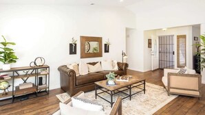 A spacious living room with a brown leather sofa, a wooden coffee table, and a bookshelf.