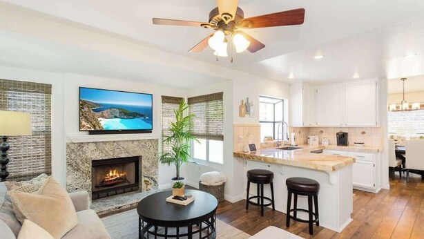 A modern living room with a fireplace, a large TV, and a ceiling fan.