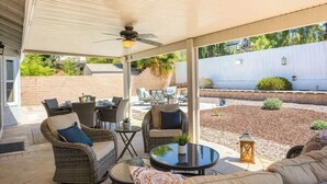 An outdoor patio area with wicker furniture, a ceiling fan, and a view of a backyard.