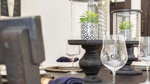 A dining table set with clear glass vases, wine glasses, and woven placemats.