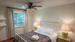 Ein Schlafzimmer mit einem Bett, zwei Nachttischen mit Lampen, einem Deckenventilator, einem Fenster mit Vorhängen und einer Heizung.