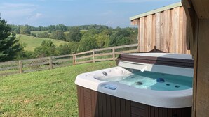 Ein Whirlpool auf einer Holzterrasse mit Blick auf sanfte Hügel und einen Holzzaun.