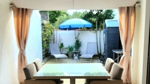 Un espacio de patio cubierto con mesa y sillas, una sombrilla azul y plantas en macetas.