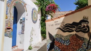 Una calle estrecha con un edificio blanco que presenta arte en mosaico y una puerta azul.