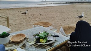 Una mesa en la playa con comida, una copa de vino y vistas a la playa y al horizonte de la ciudad.