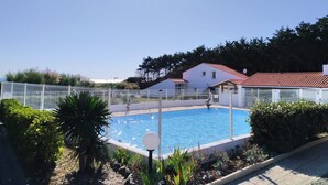Una piscina rodeada por una valla blanca, con una casa al fondo y árboles alrededor.