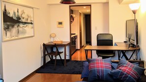 Un espacio habitable compacto con cama, escritorio, silla y kitchenette pequeña.