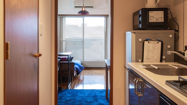 Un pasillo estrecho que conduce a un comedor con alfombra azul, una cocina con microondas y una puerta de madera.