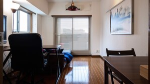 Una habitación con piso de madera, una mesa de comedor, una silla negra, un sofá y un ventanal con persianas.