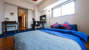 Un dormitorio con cama, escritorio, silla, televisión y ventana.