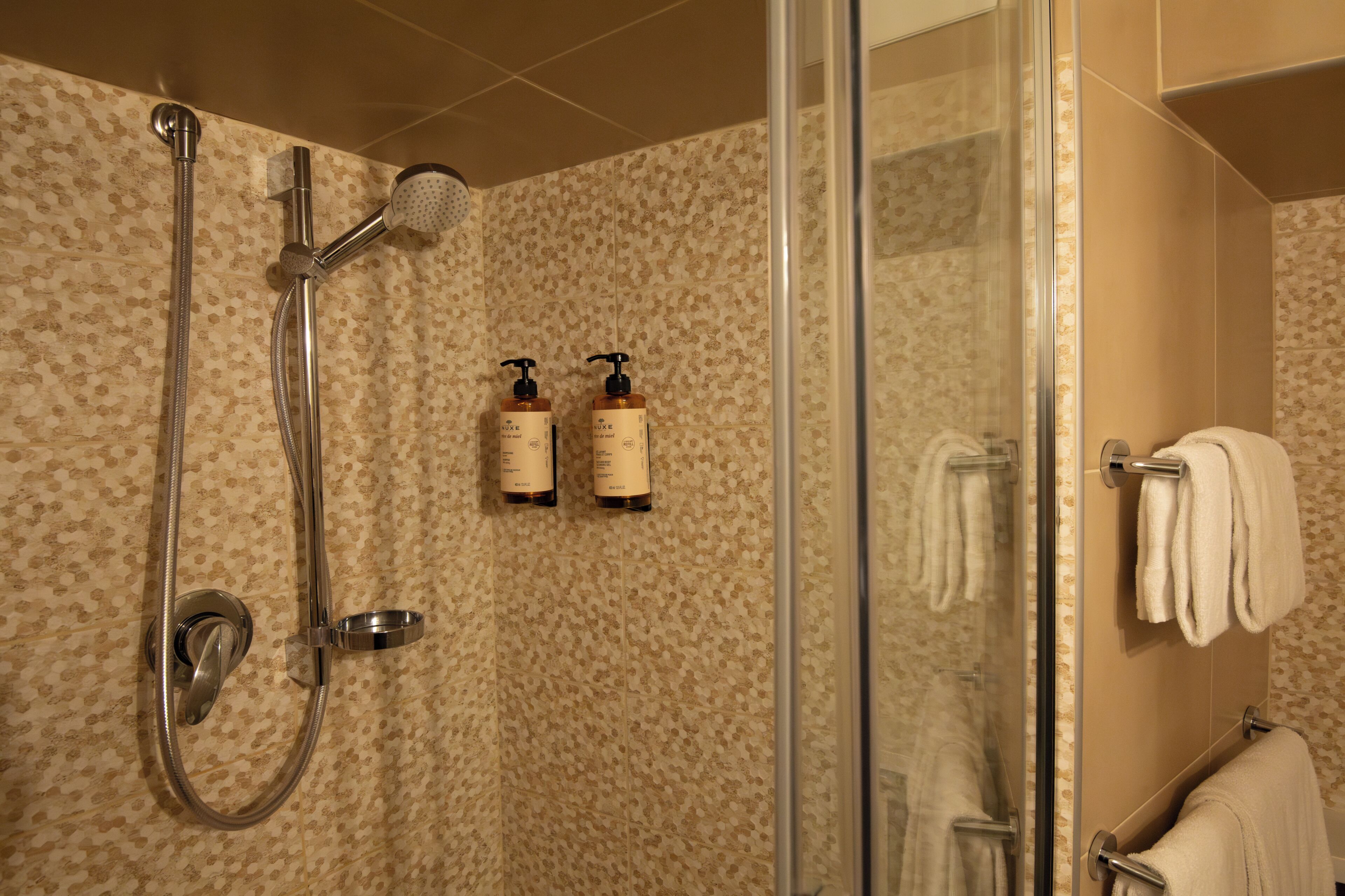 A shower with a glass door, a handheld showerhead, and two bottles of shampoo.