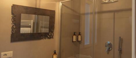 Une salle de bain avec une douche à parois de verre, un lavabo blanc, un miroir et un luminaire au design géométrique.