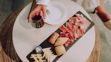 A round table with a white plate, a glass of red wine, a cheese board with various cheeses, and a selection of cured meats.
