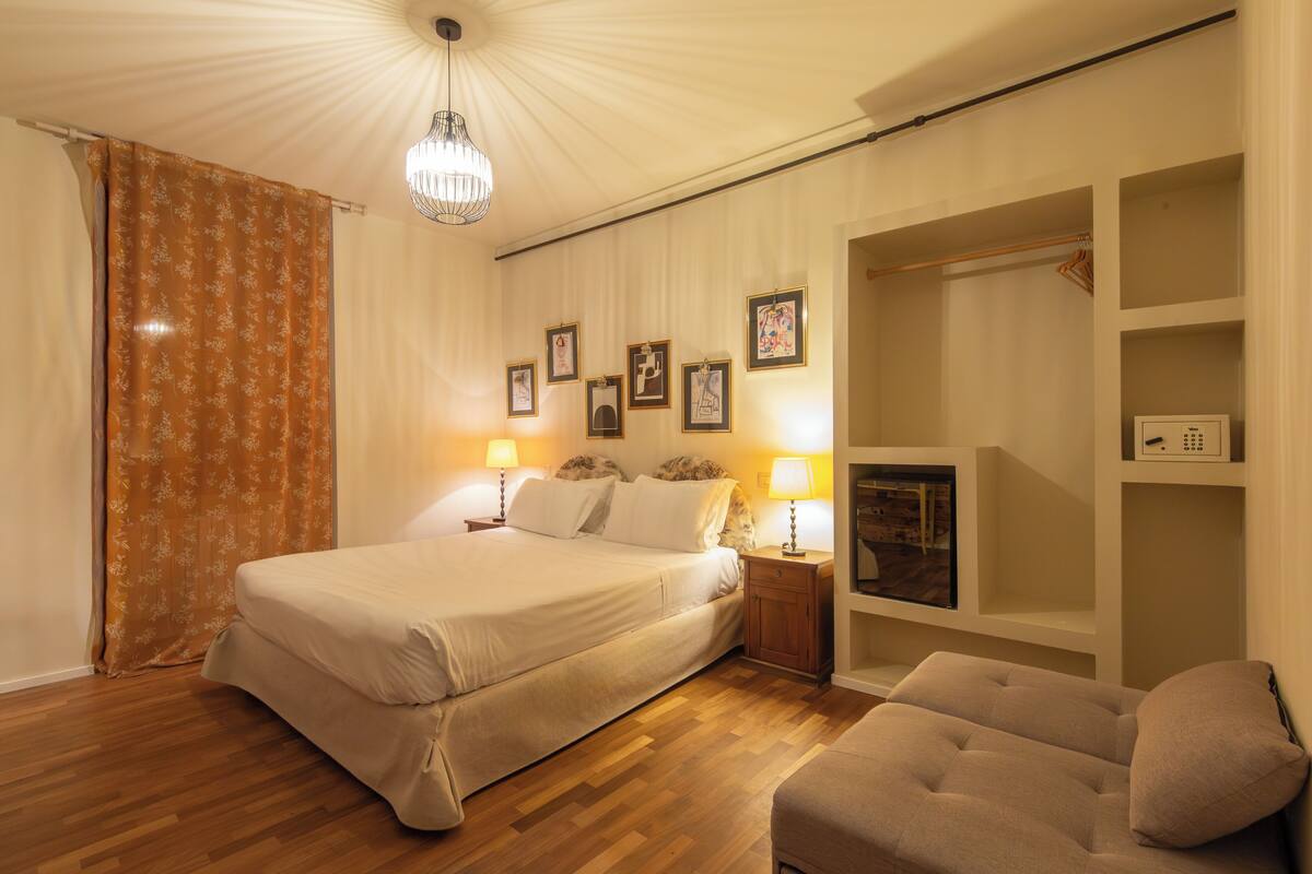 Ein Schlafzimmer mit einem Bett, Nachttischlampen, einem Kleiderschrank und einem Sessel.