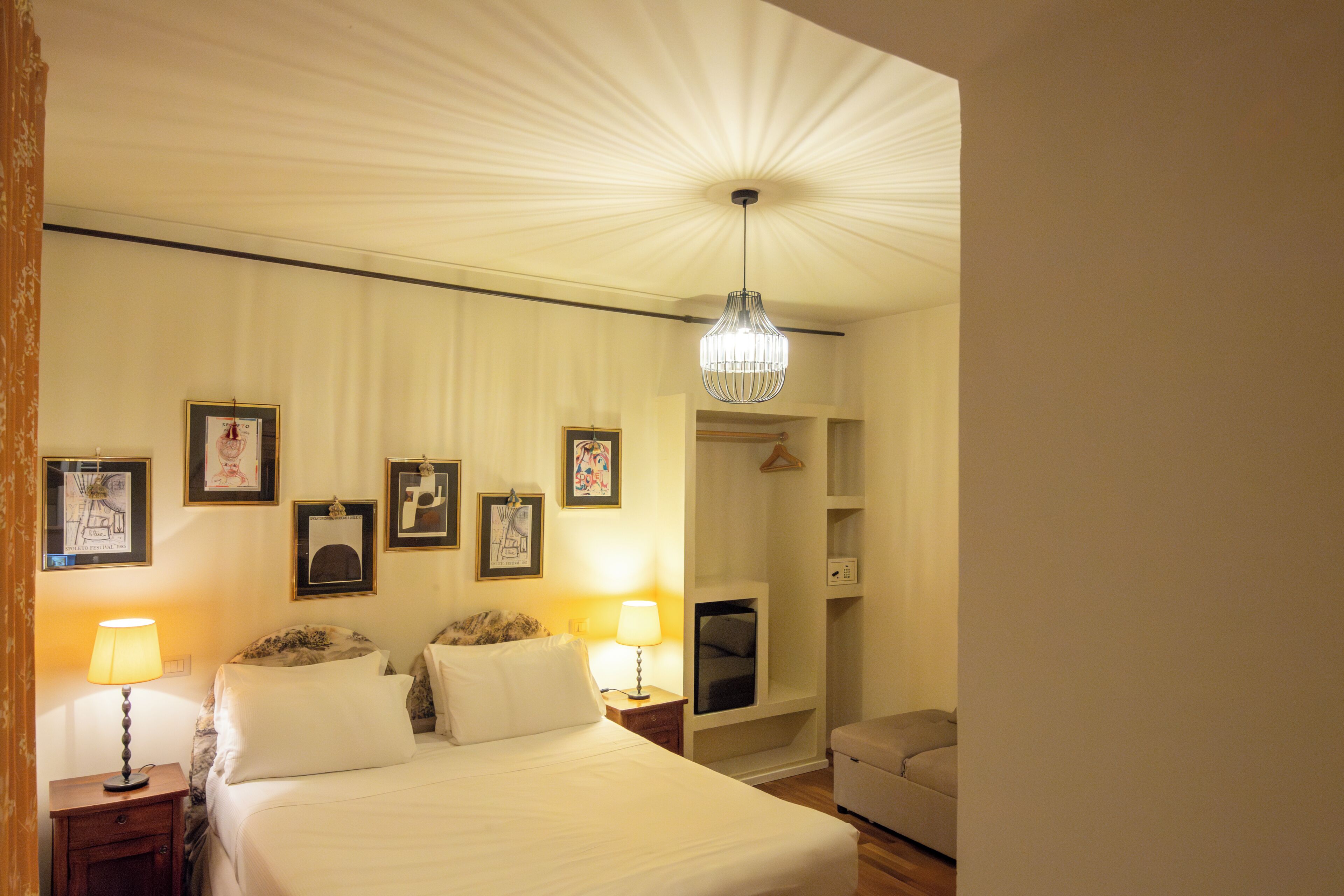 A hotel room with a bed, bedside lamps, a TV, a sofa, and framed pictures on the wall.
