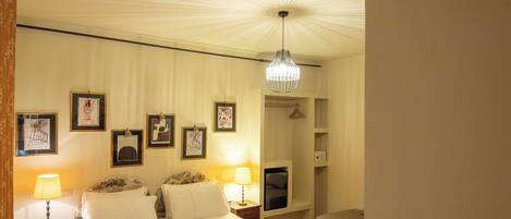 A hotel room with a bed, bedside lamps, a TV, a sofa, and framed pictures on the wall.