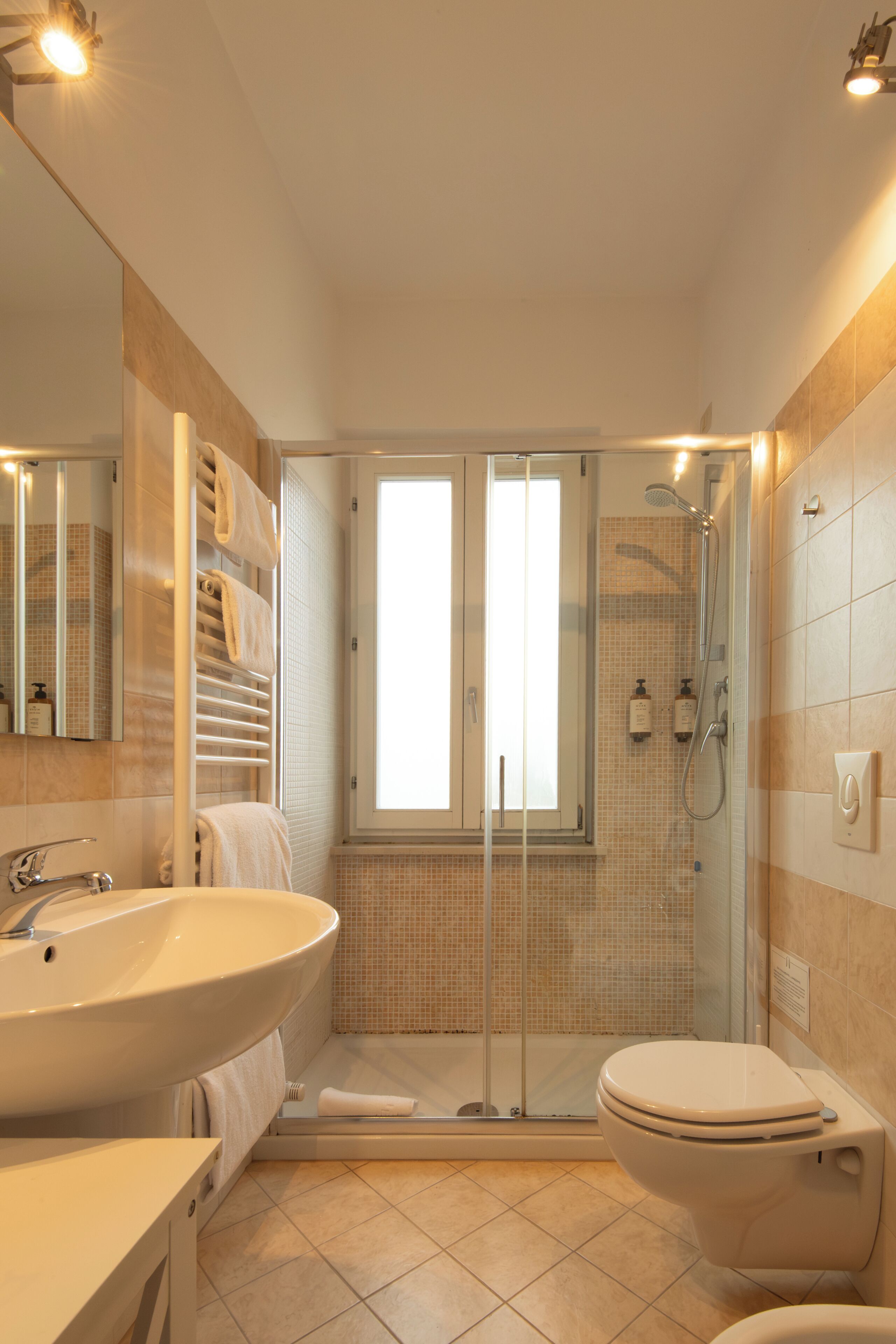 A bathroom with a large sink, a toilet, a glass shower enclosure, and a window.